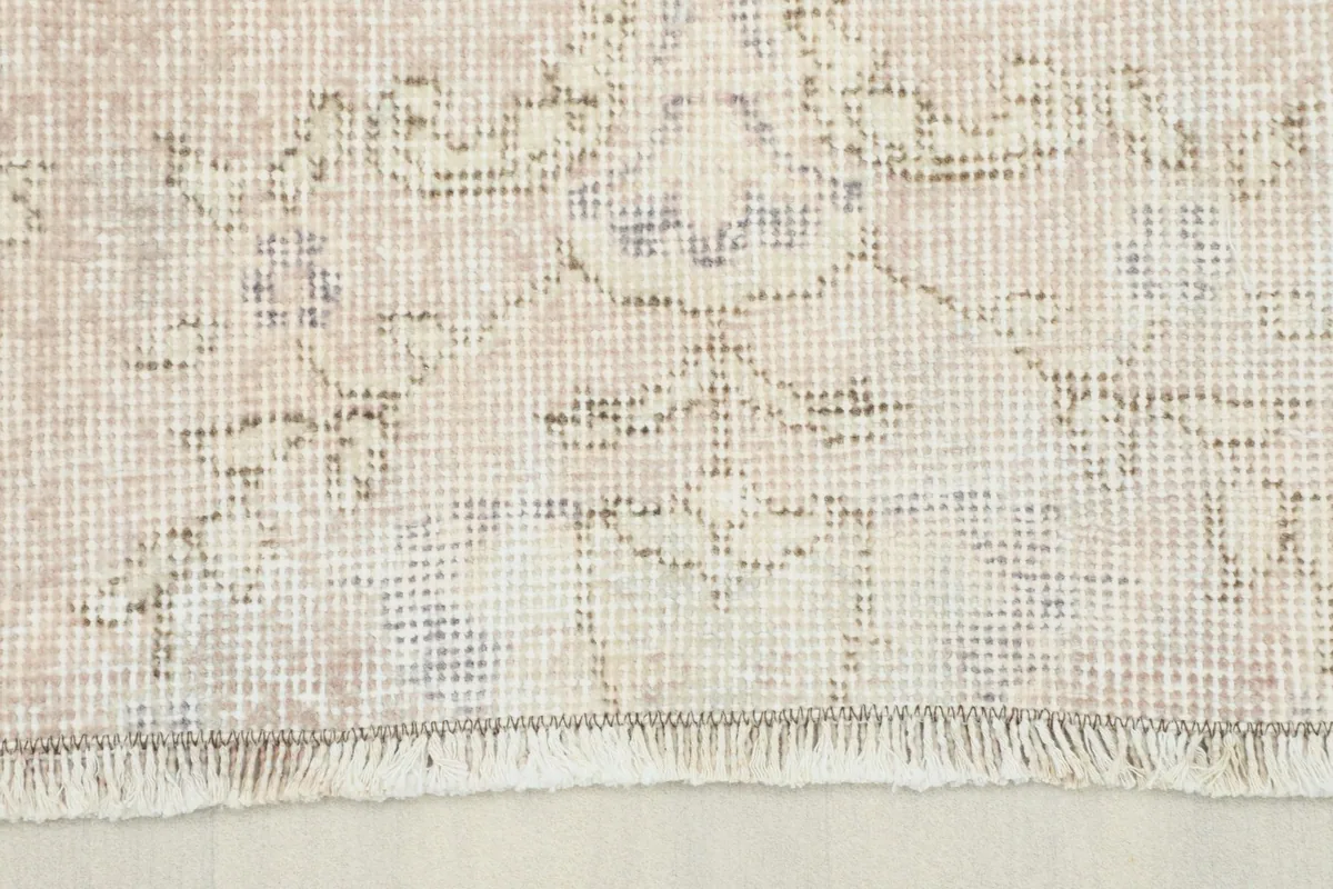 Close-up view of the rug's edge, showing the low pile and faded rose and ivory tones.