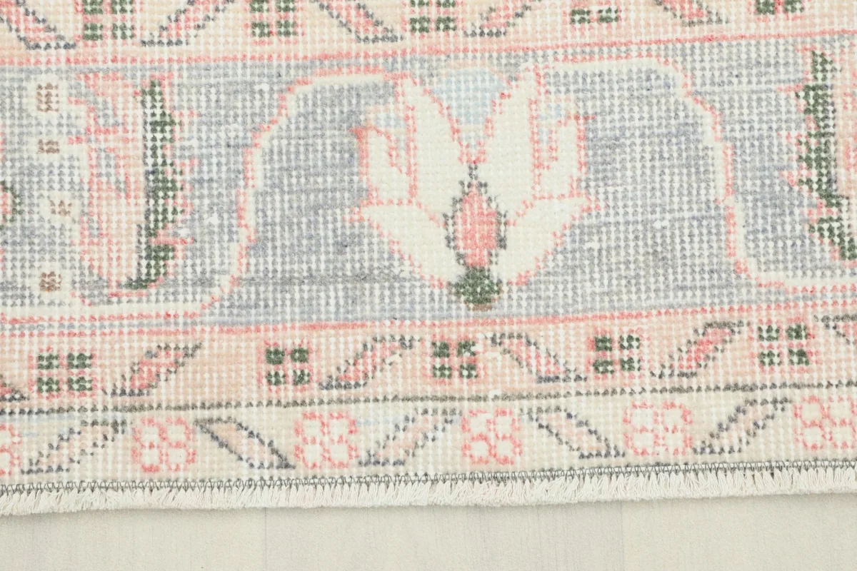 Close-up of the rug's border showing gray, rose, and ivory tones with intricate patterns.