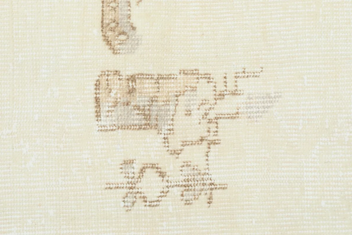 Close-up of a beige floral and vine motif on the cream wool pile, highlighting the hand-knotted texture.