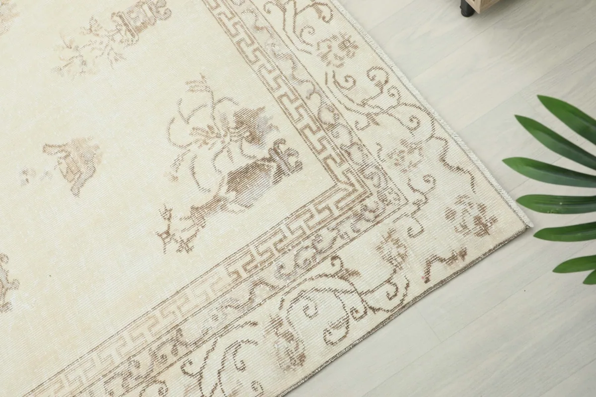 Detail of the rug's border, featuring intricate beige patterns and a Greek key design against the cream field.