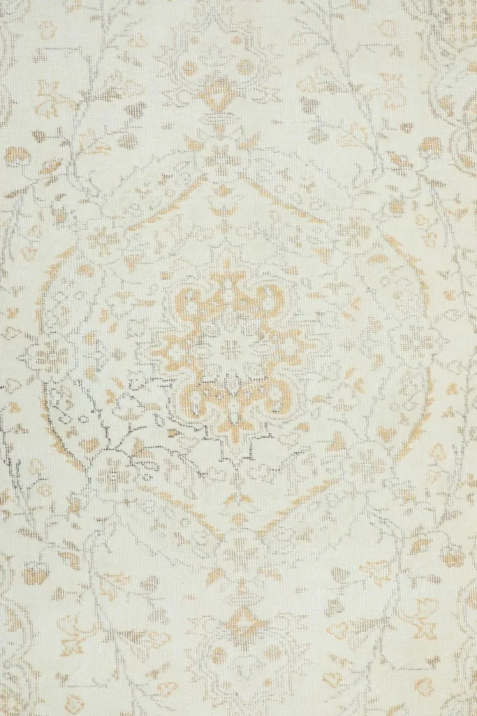 Detailed overhead shot of the rug's central medallion and surrounding floral motifs in ivory, gold, and gray.