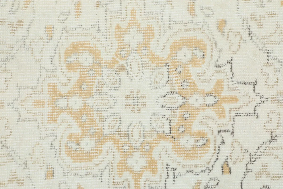Macro detail of the rug's wool pile, showing the texture and faded gold and gray patterns.