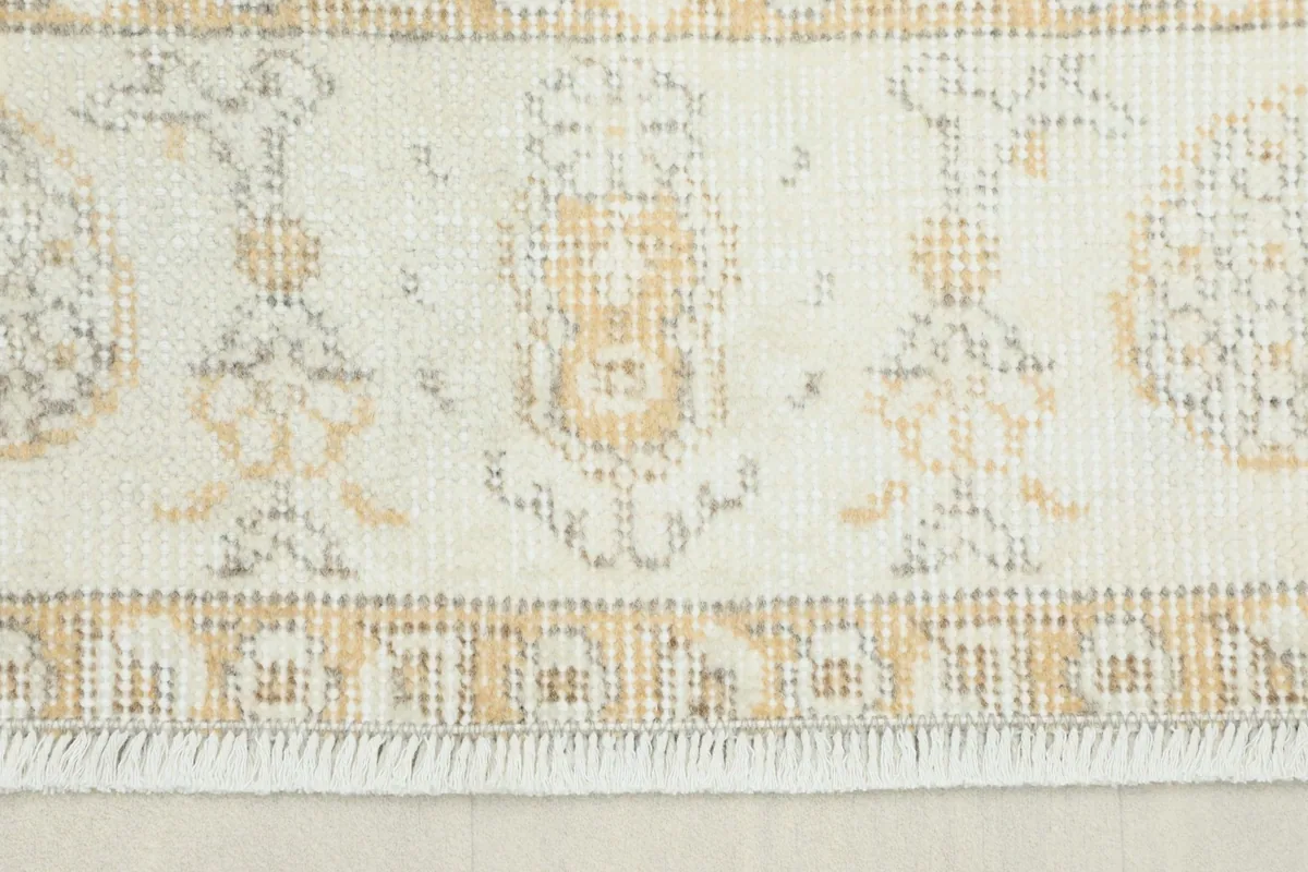 Close-up view of the intricate beige and gold patterned border and fringe of the hand-knotted rug.