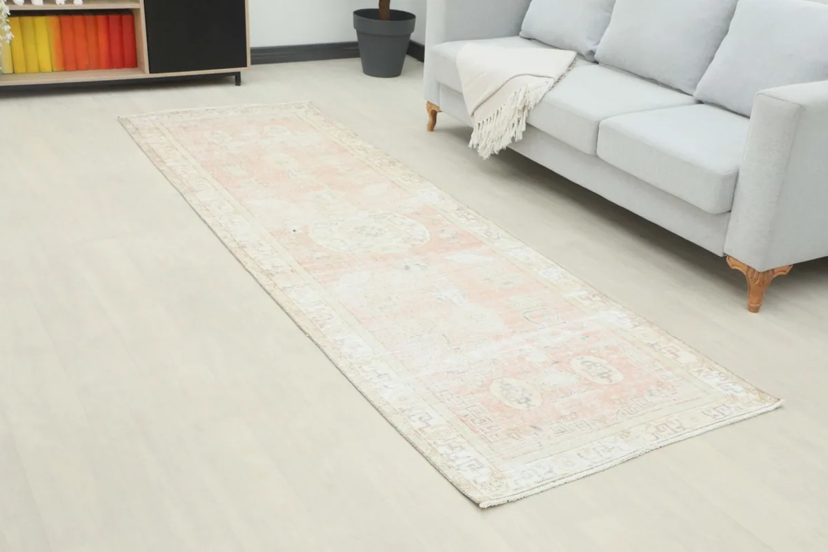 Angled view of the runner rug in a room, highlighting its distressed rose and ivory colors.