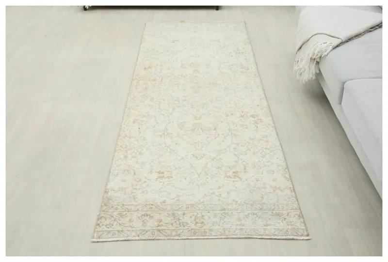 Full top view of the 2'11" x 8'5" cream and tan floral vintage runner rug on a white floor.