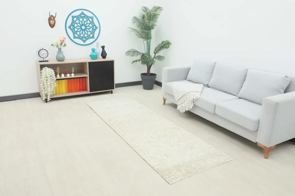 Vintage runner rug displayed in a living room setting next to a sofa and cabinet, showing its scale.