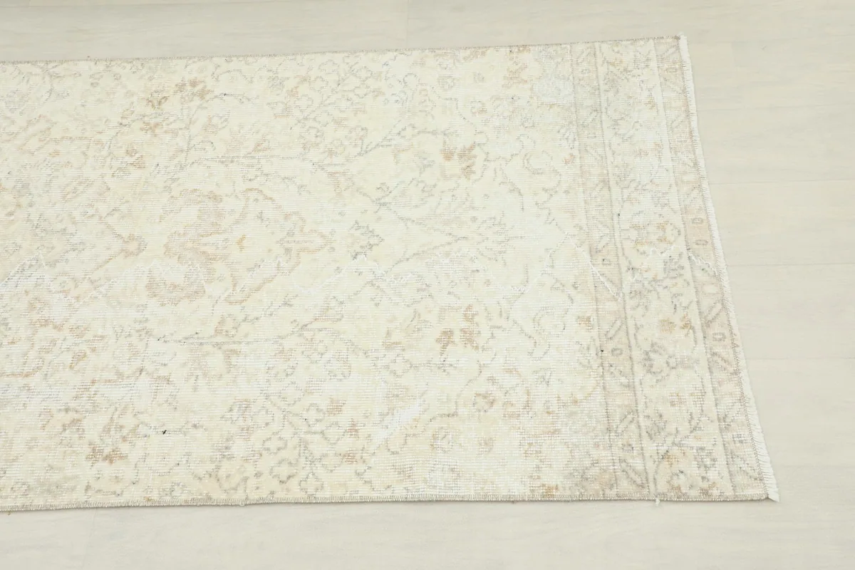Close-up detail of the rug's side, showing the cream field and faded tan floral patterns.