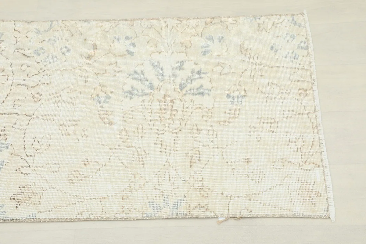 Close-up detail of the rug's subtle floral pattern with ivory, blue, and tan tones.