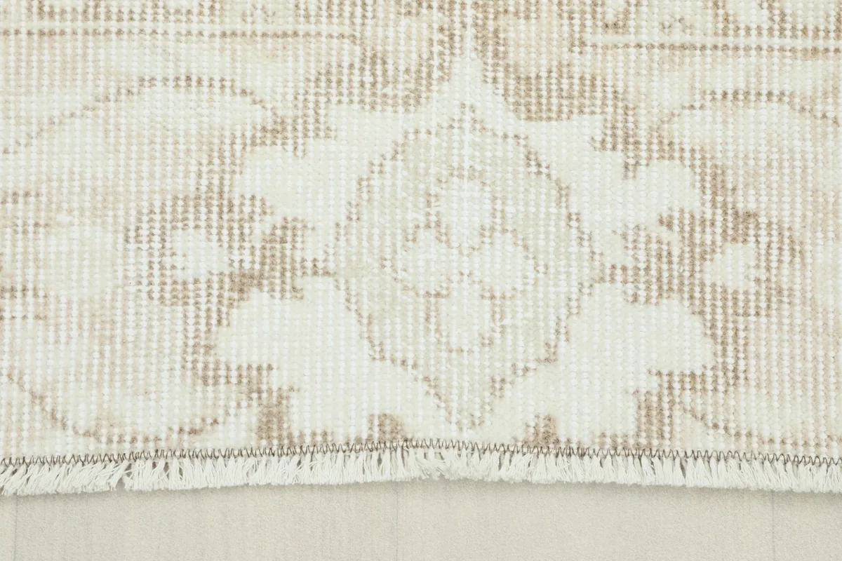 Close-up view of the rug's short fringe and a section of the beige patterned border.