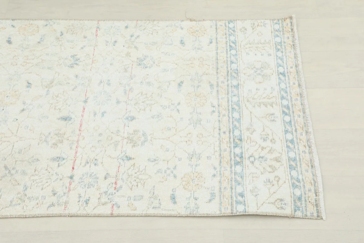 Close-up view of one end of the rug, showing the cream field and blue geometric border.