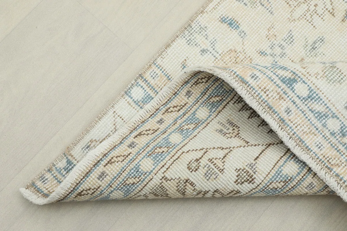 Corner of the rug folded back, revealing the cotton foundation and reverse side of the knots.