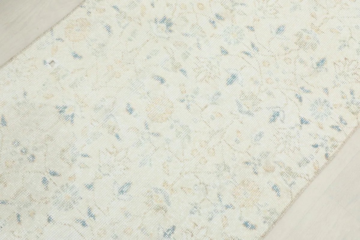 Overhead detail of the rug's cream field with subtle blue and tan floral motifs.