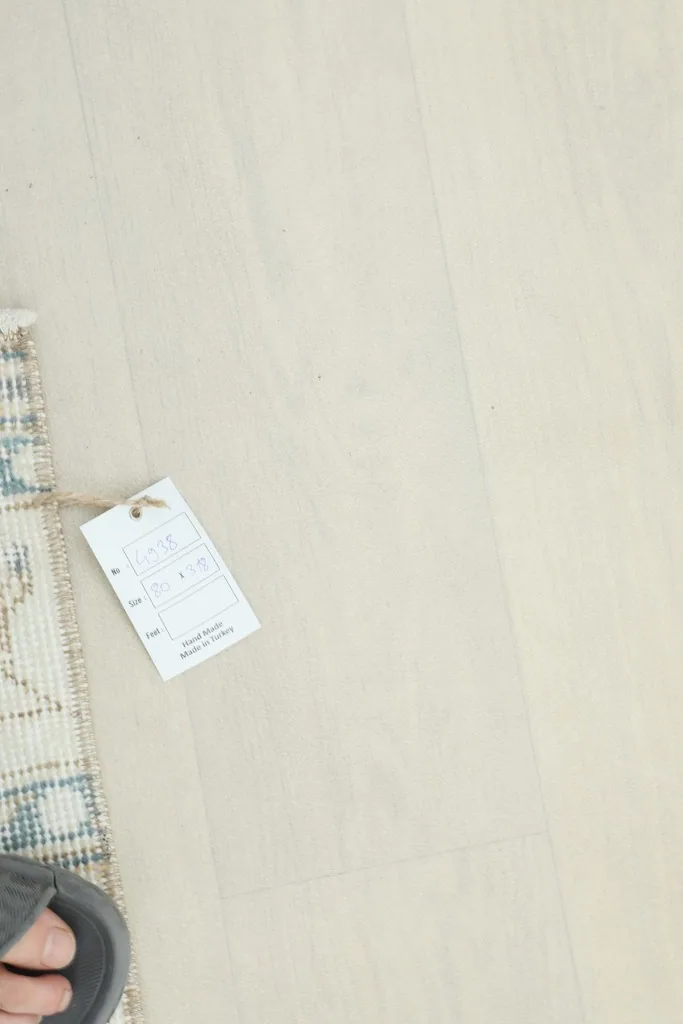 A partial view of the rug with a tag attached, on a light wooden floor.