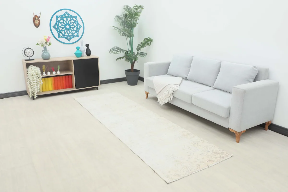 Vintage runner rug displayed in a living room setting next to a gray sofa and wooden cabinet.