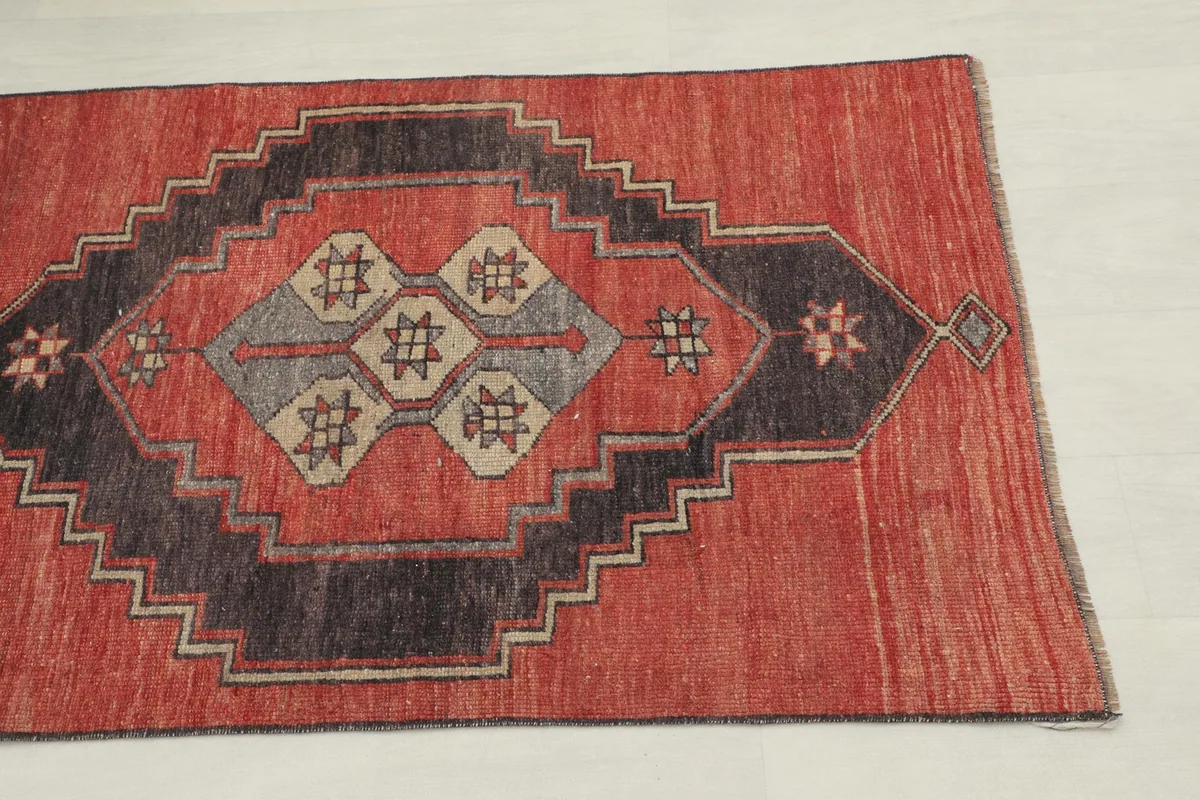 Close-up detail of one end of the rug, showing the rust field and charcoal, gray, tan motifs.
