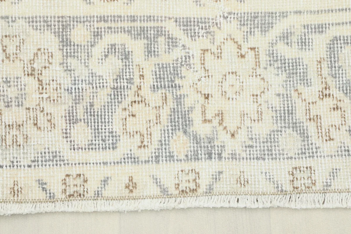 Close-up detail of the rug's border and fringe, highlighting the gray geometric patterns and ivory tones.