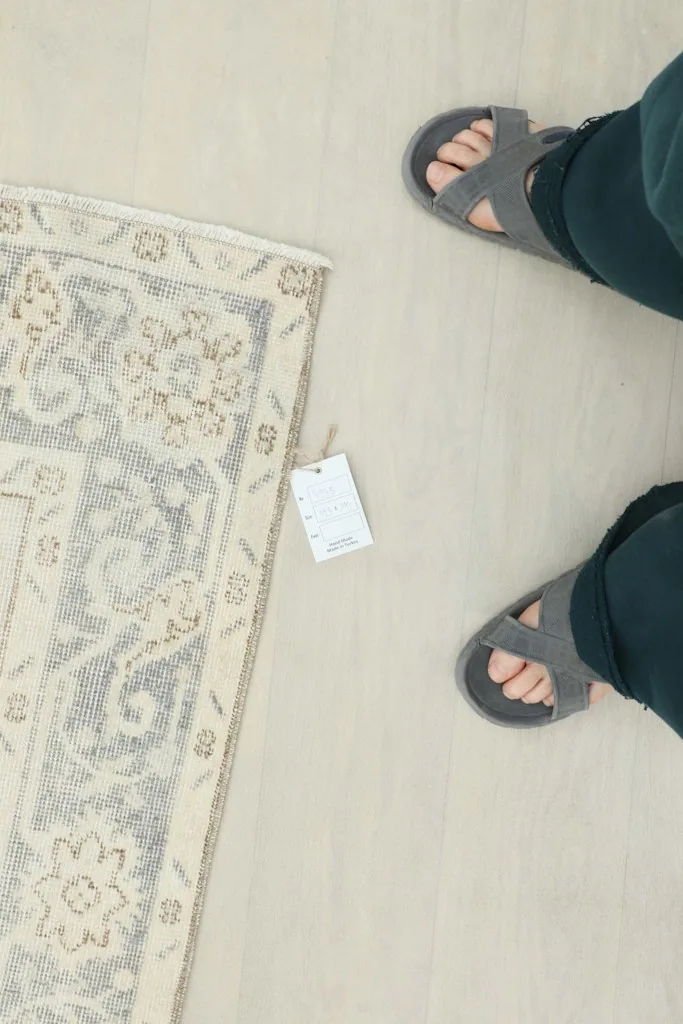 Overhead view of a section of the rug next to feet, indicating scale and the attached product tag.