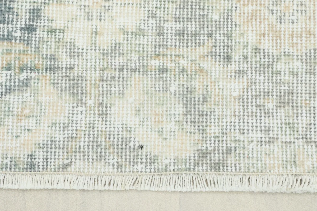 Close-up detail of the rug's faded blue, beige, and gray wool pile with fringe.