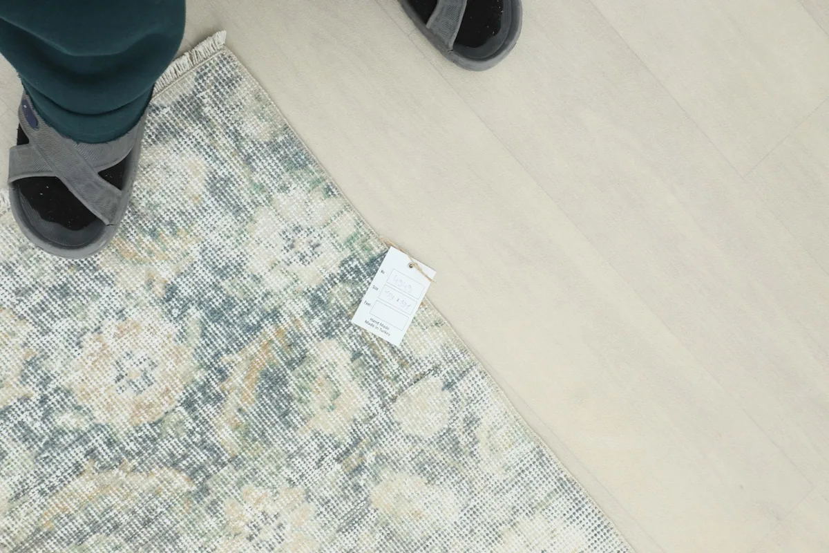 Overhead view of a section of the rug with a size tag, showing feet for scale.