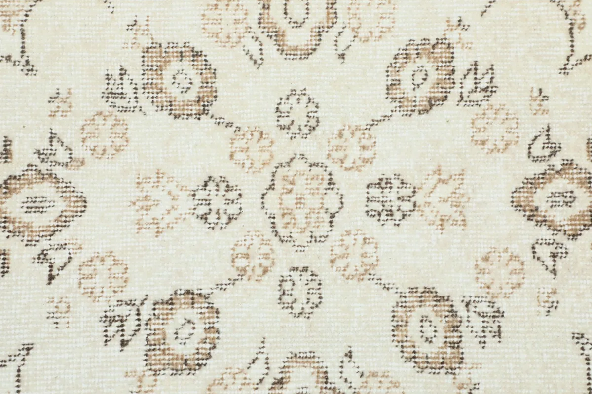 Close-up of the rug's field showing repeating floral patterns in brown and tan on an ivory background.