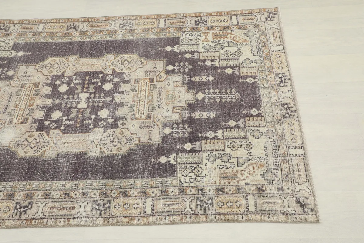 Close-up view of the corner and border of the charcoal geometric rug, highlighting distressed areas.