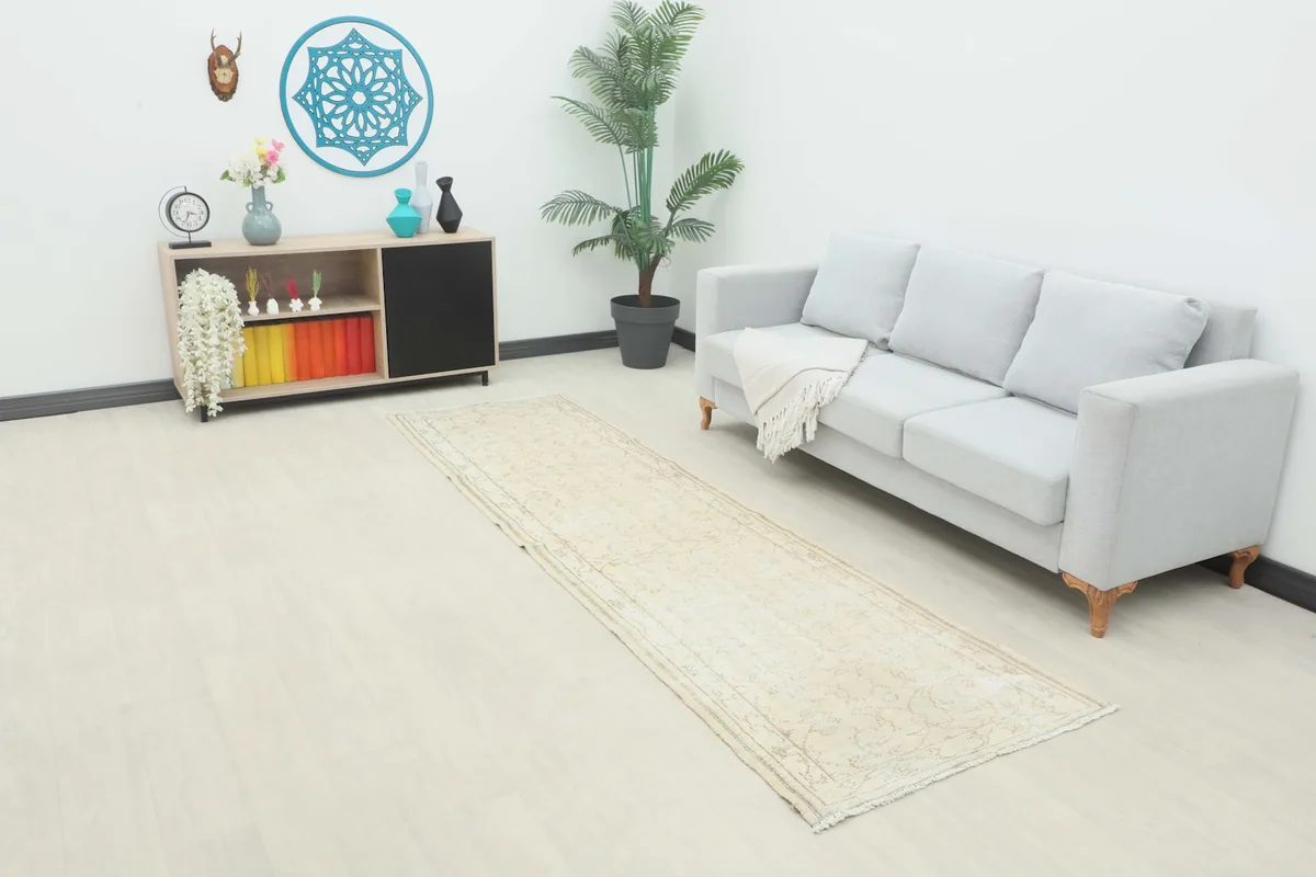 Vintage cream runner rug displayed in a modern room setting next to a gray sofa and plant.