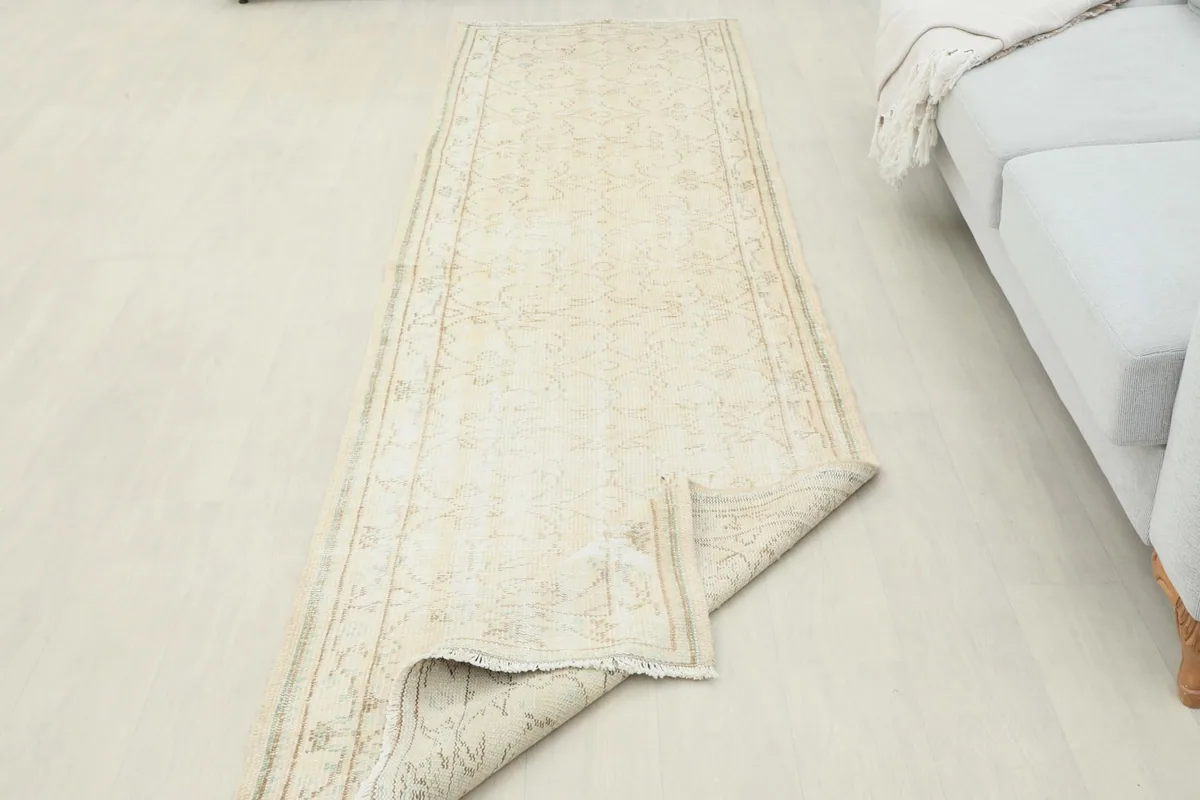 Cream runner rug with one end folded back, showing the back of the rug and its texture.