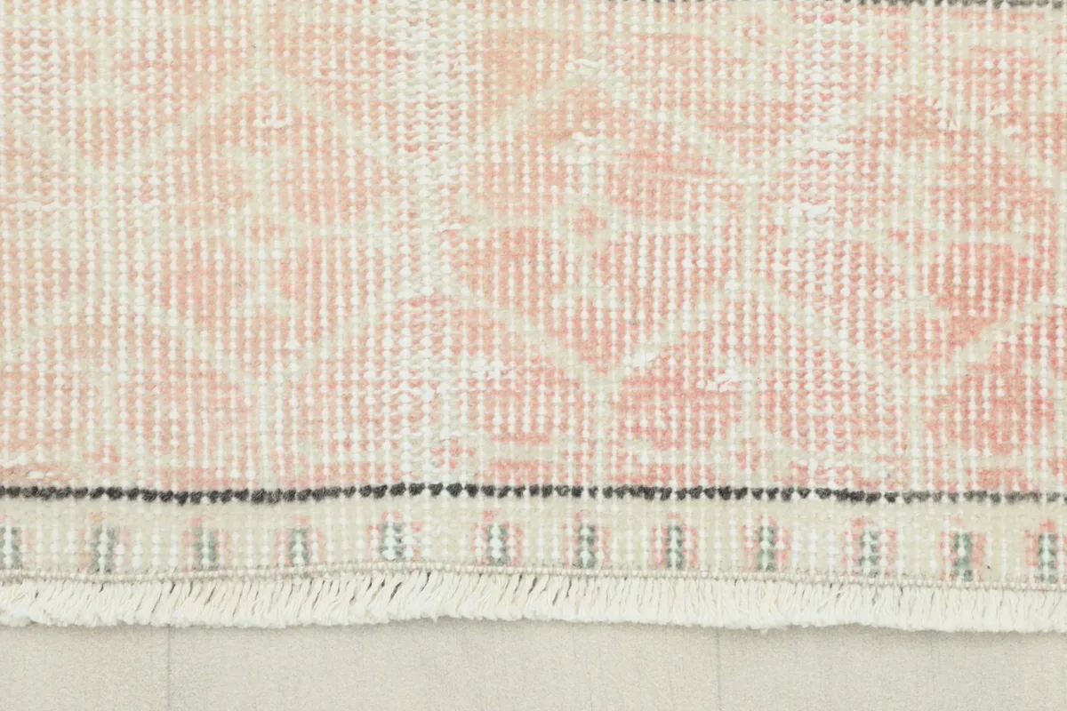 Close-up detail of the rose colored border with geometric patterns and fringe