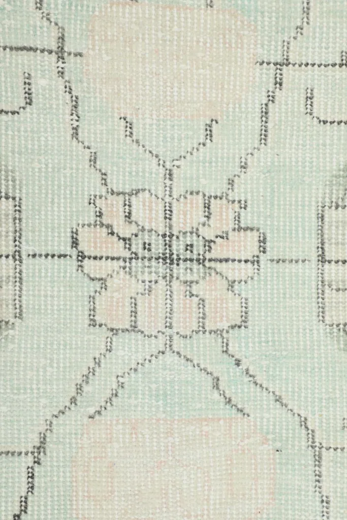 Close-up of the faded floral motif and texture within the rug's cream field