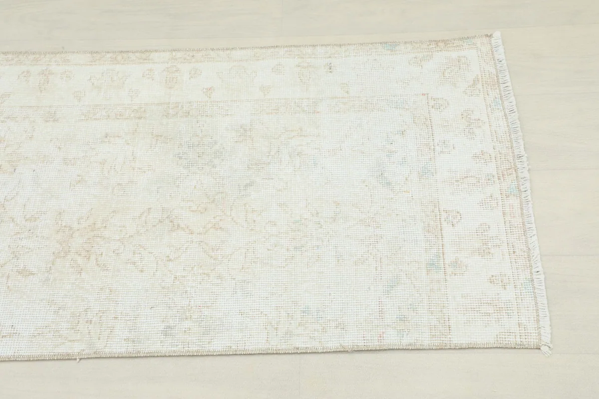 Close-up view of the faded ivory and beige geometric and floral motifs on the runner rug.