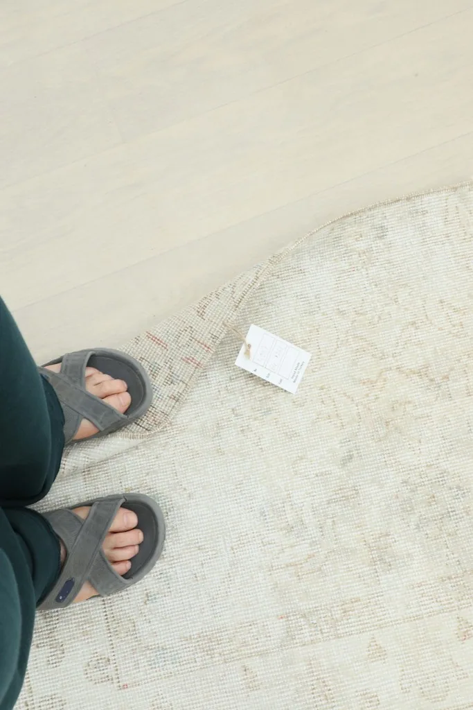 Overhead view of feet on the floor next to a corner of the rug, showing scale.