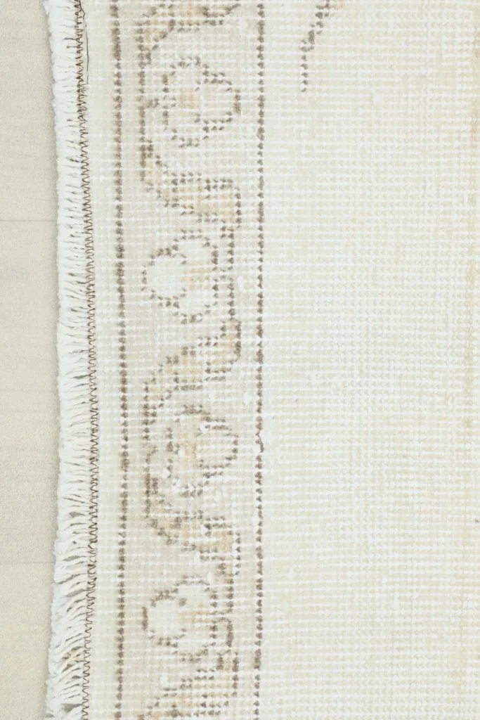 Close-up detail of the geometric border and fringe of the ivory vintage rug
