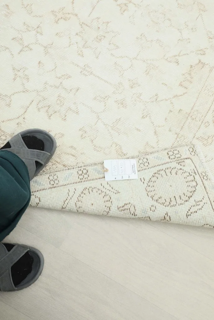 Person's feet next to the rug's reverse side, showing the tag and the rug's backing.