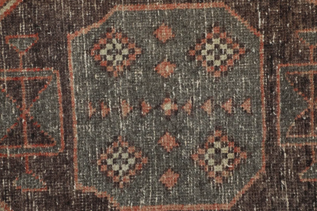 Extreme close-up of a charcoal and rust geometric motif within a medallion, showing individual knots
