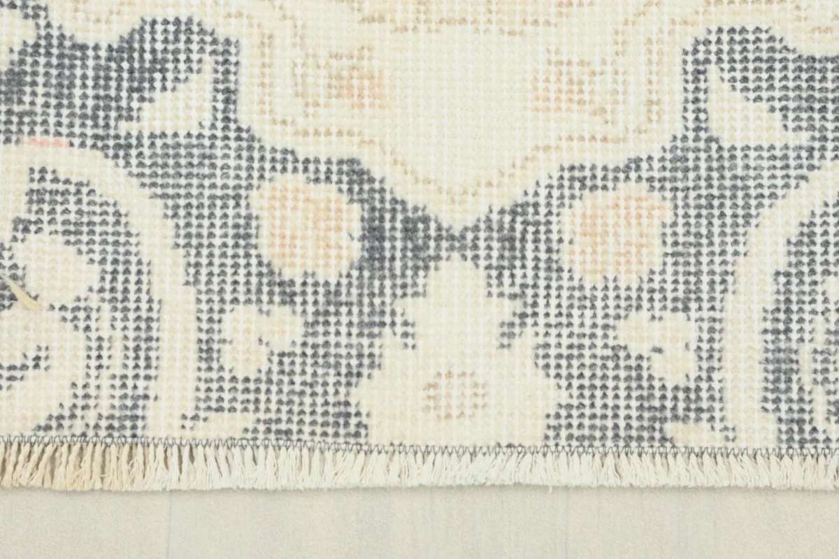 Close-up detail of the rug's border showing gray and ivory motifs and short fringe.