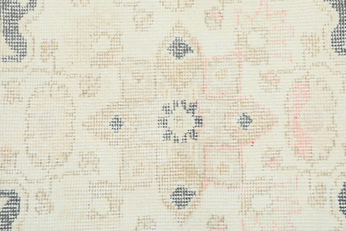 Close-up of the low wool pile showing intricate knotting and faded rose and tan hues.