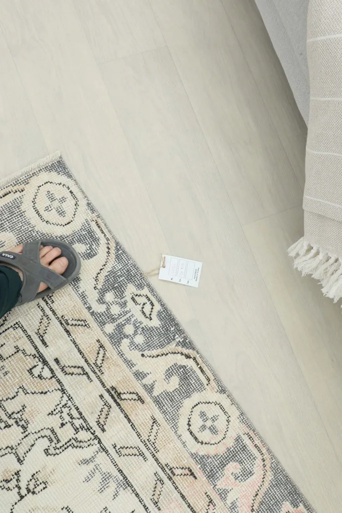 Overhead view of a corner of the rug with a tag, showing the border design and a foot for scale.