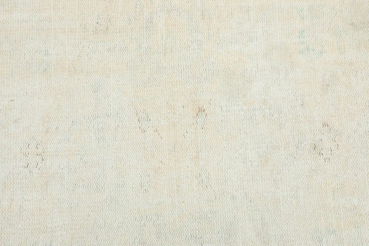 Detailed view of the faint, ghost-like geometric patterns and color variations within the ivory rug.