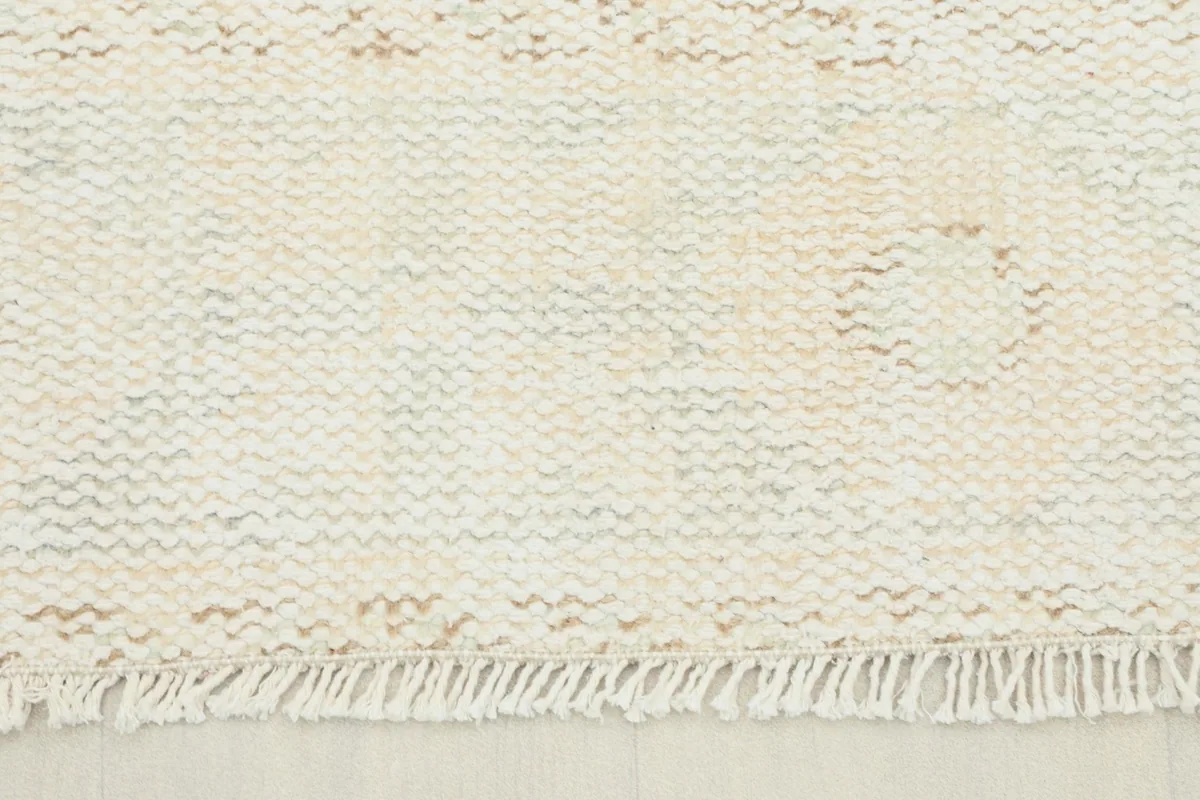 Close-up view of the low wool pile texture and subtle ivory and tan variations on the rug surface.