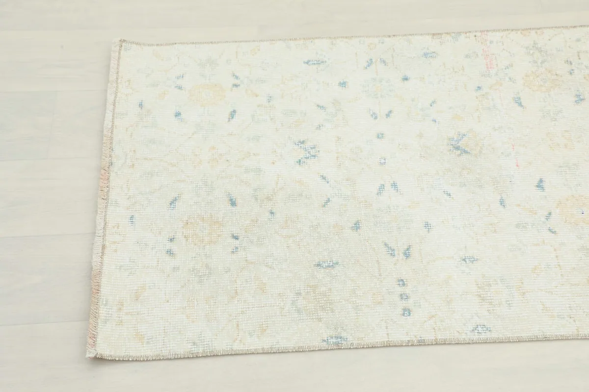 Close-up of the rug's field, highlighting the faded blue and tan floral motifs on an ivory background.