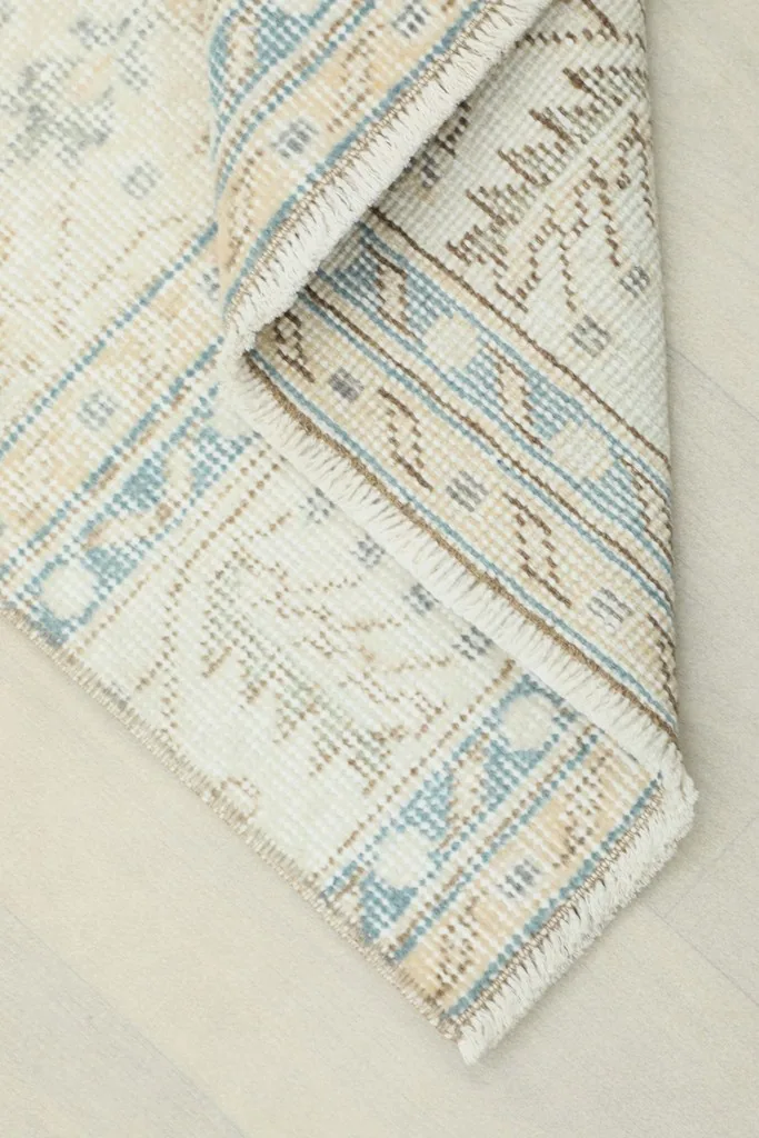 Corner of the rug folded back, showing the cotton foundation and the reverse side of the knotting.