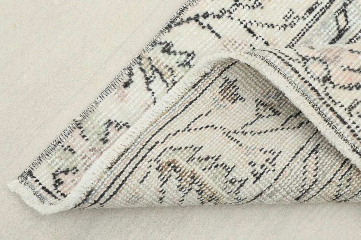 Corner of the rug folded back, revealing the fringe and texture of the wool pile.