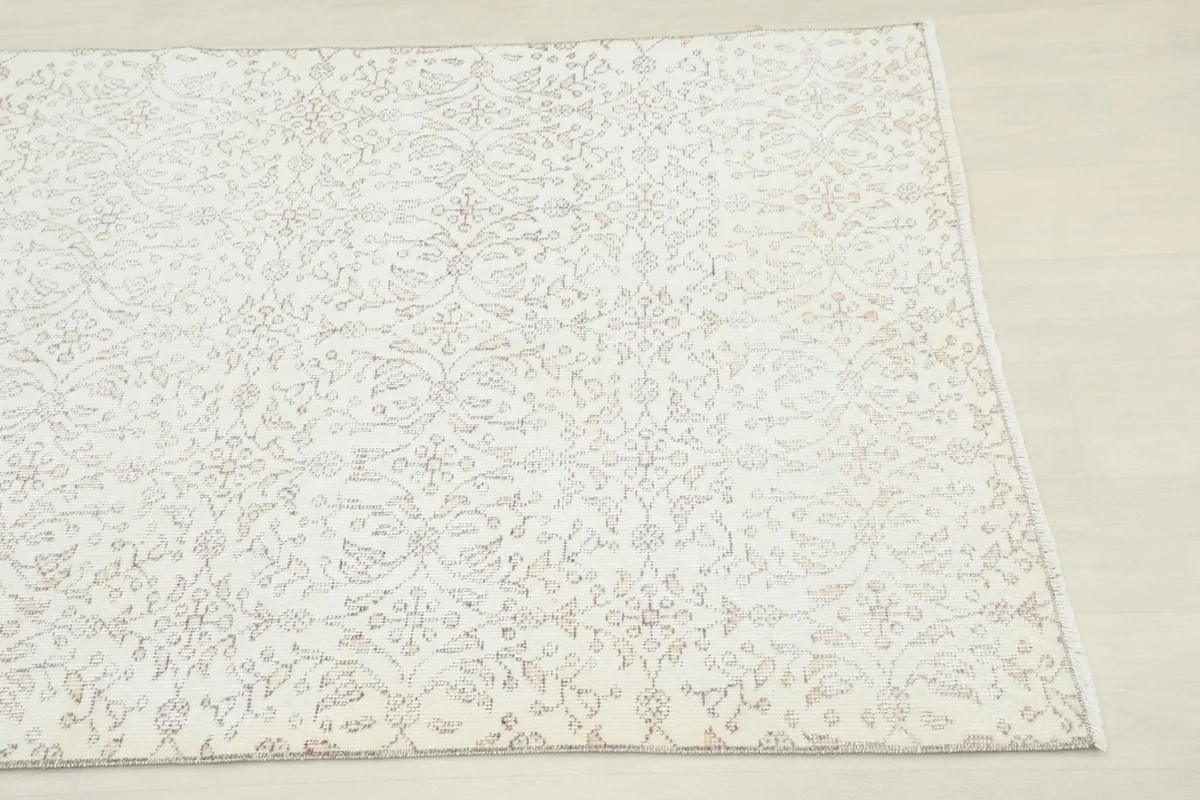 Close-up detail of the vintage rug's corner, highlighting the subtle tan floral motifs.