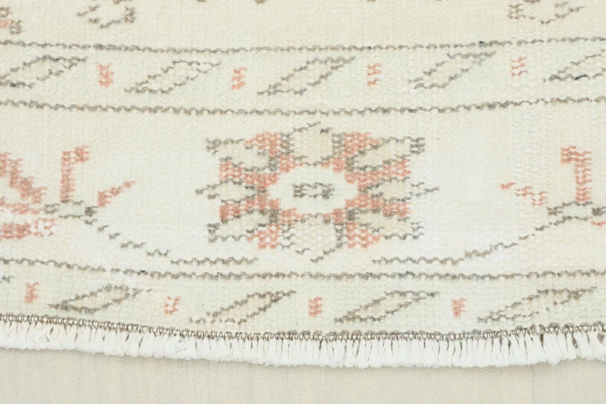 Close-up detail of the rug's short fringe and border, showing rose and gray geometric patterns.