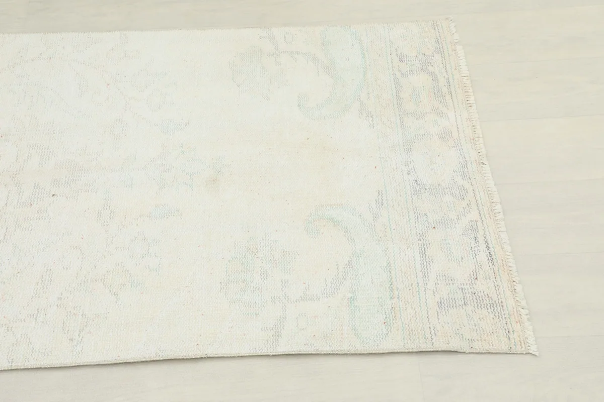 Close-up view of the rug's end, highlighting the subtle cream, blue, and green colors and faded border