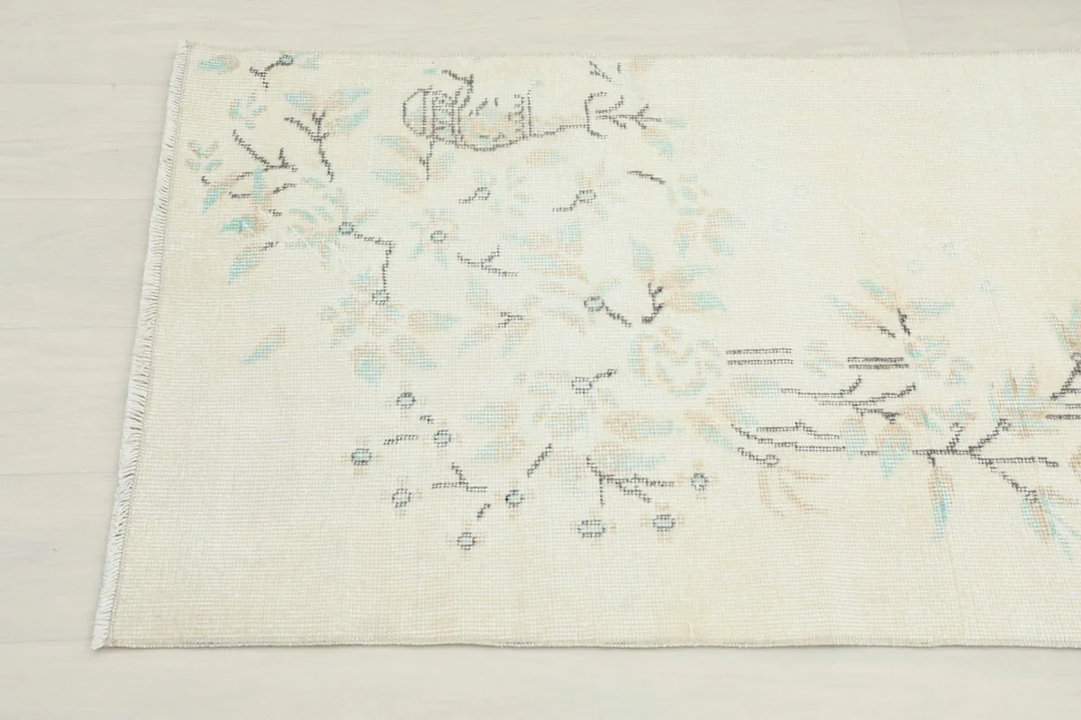 Detailed view of the botanical and floral motifs in beige and gray on the ivory rug field