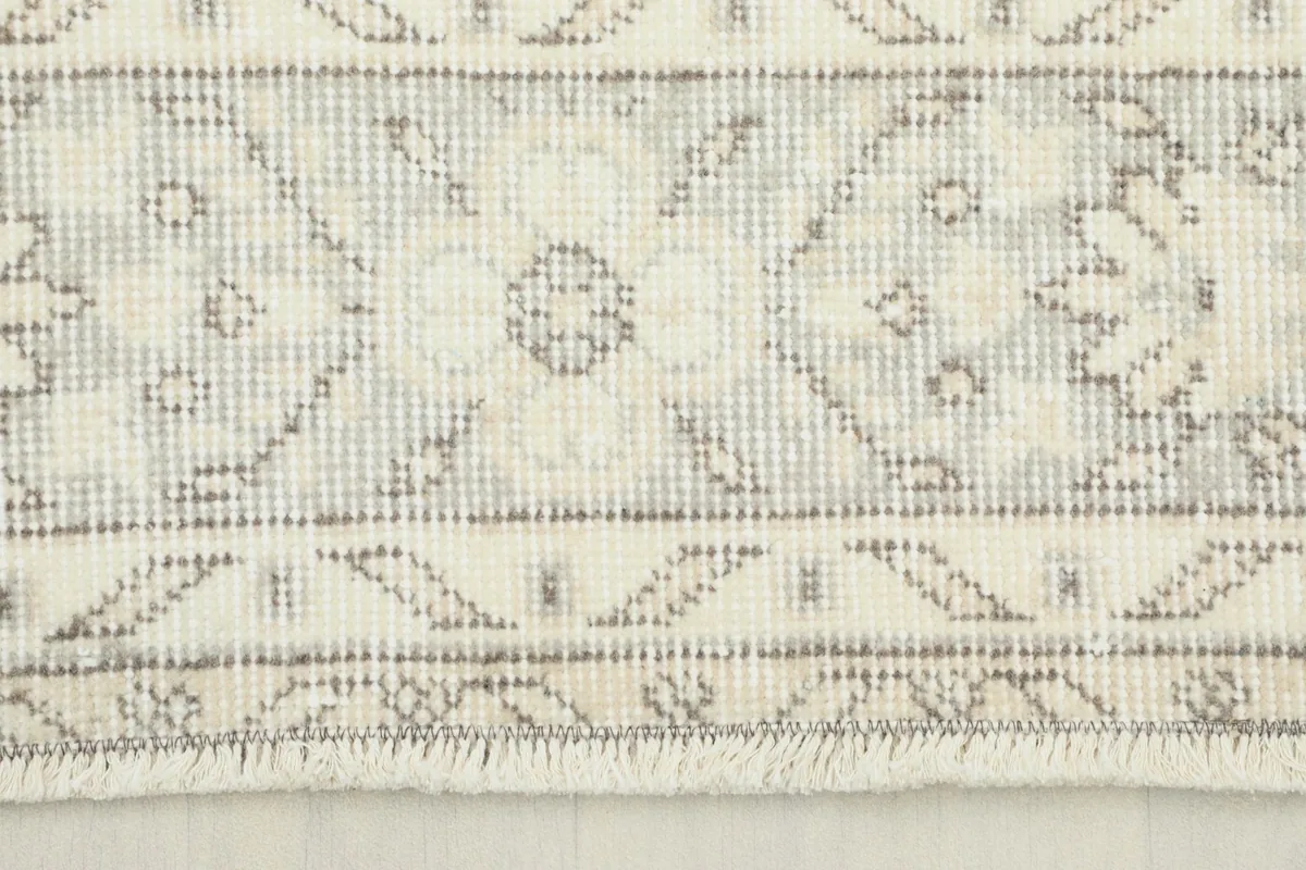 Close-up view of the rug's short fringe and subtle pattern details in ivory, gray, and tan