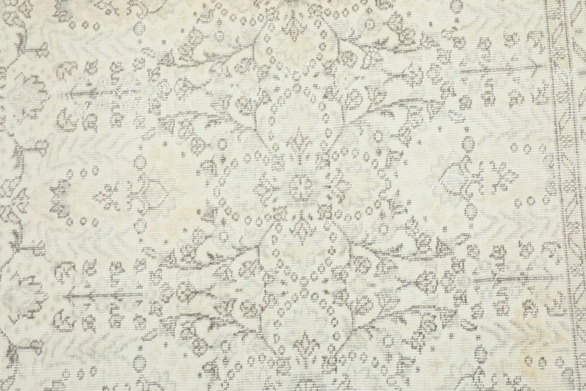 Detailed view of the central floral and geometric motifs in faded gray on an ivory field
