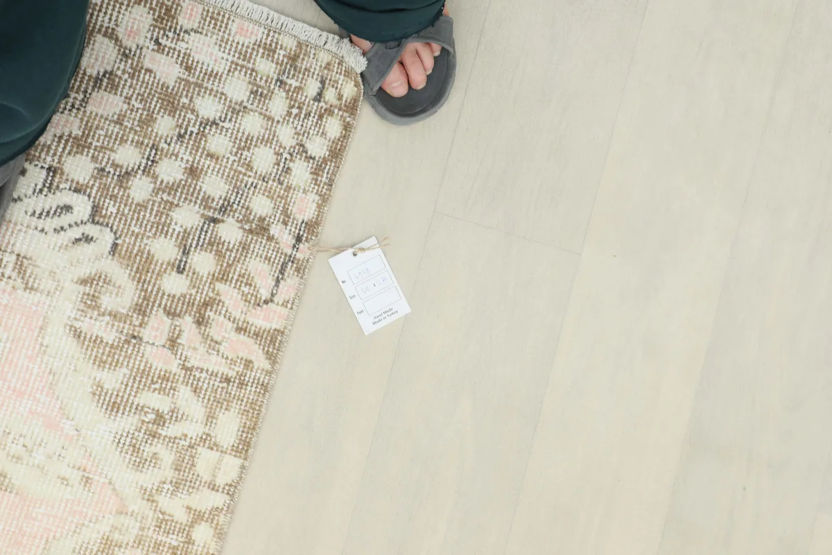 View of the Soft Rose Floral Medallion Rug's edge with a tag, showing the texture and fringe.