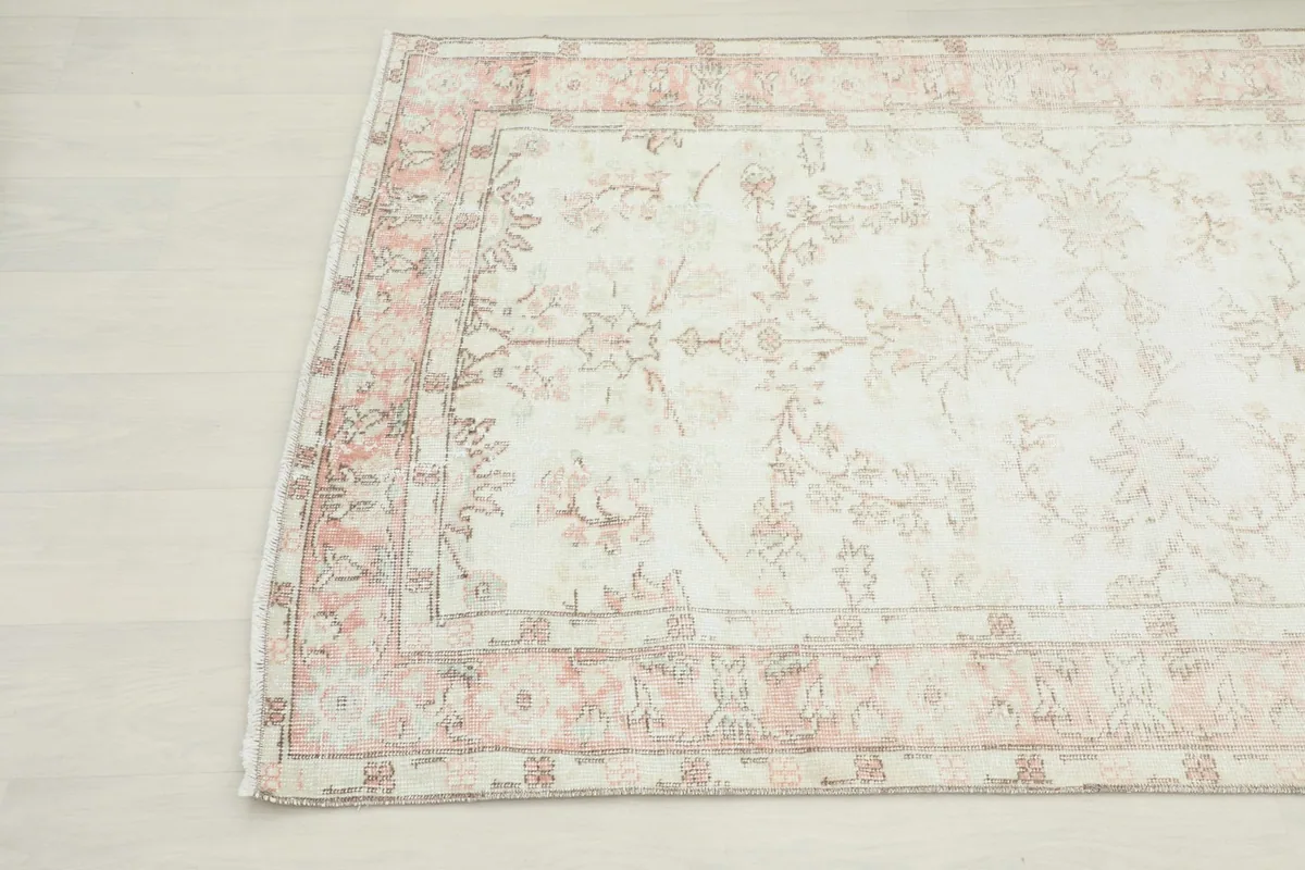 Angled view of the rug's top left corner, showing the faded rose tones.